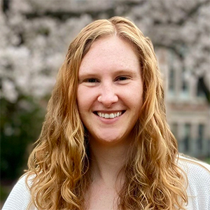 Headshot of Kim Ingraham, who is smiling while standing in front of the cherry blossoms on UW's campus. She is a white woman with long wavy strawberry blonde hair.