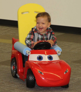 Toddler laughing and playing in a riding toy car adapted by Go Baby Go Seattle