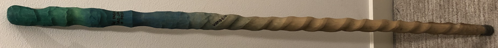 A handcarved cane with a spiral design and painted green at the top