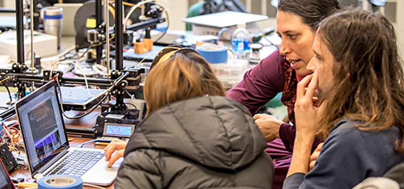 Jennifer Mankoff works with two students in a 3D printing lab crowded with tools.