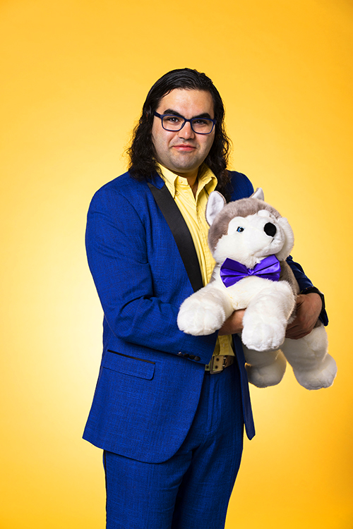 Ethan K. Gordon poses for the Husky100 photo series wearing a vivid purple suit and yellow shirt while cradling a stuffed UW Husky dog. 