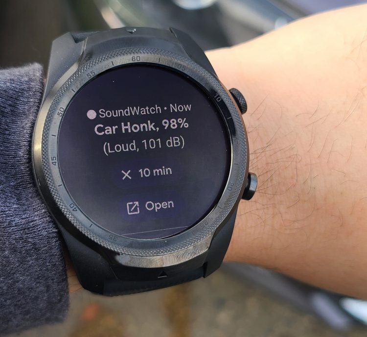alt="A wrist with a smartwatch on it. The smartwatch has an alert that says "Car honk, 98%, Loud, 101 dB" It also has options to snooze the alert for 10 minutes or open in an app on the user's phone."