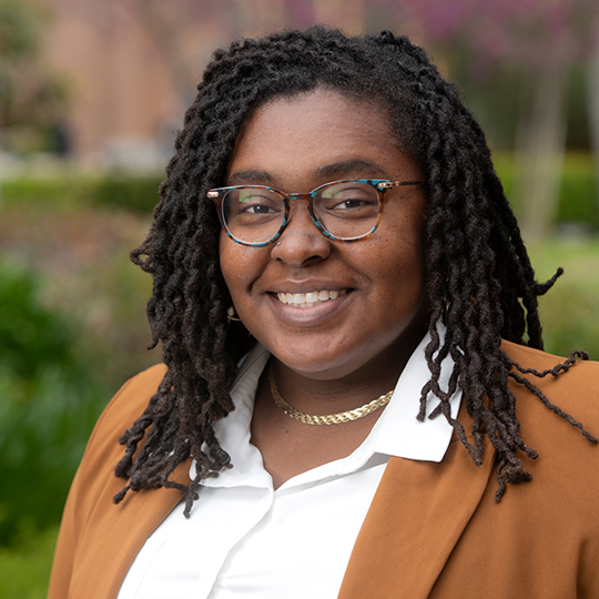 headshot of Jazette Johnson wearing a white shirt and amber colored blazer. She is smiling warmly.