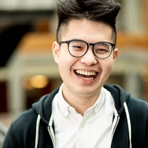 Headshot of Kevin Lin, a smiling light-skinned East Asian young adult with short black hair. He is wearing a white button down shirt and a black hoodie.