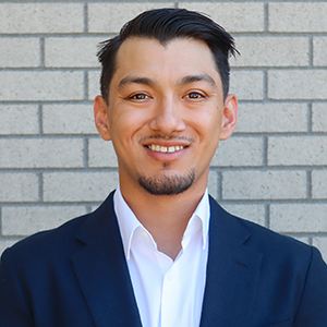 Headshot of Anthony Osuna, smiling warmly at the camera and dressed in a suit and tie. He has short, dark hair and a well-groomed appearance.