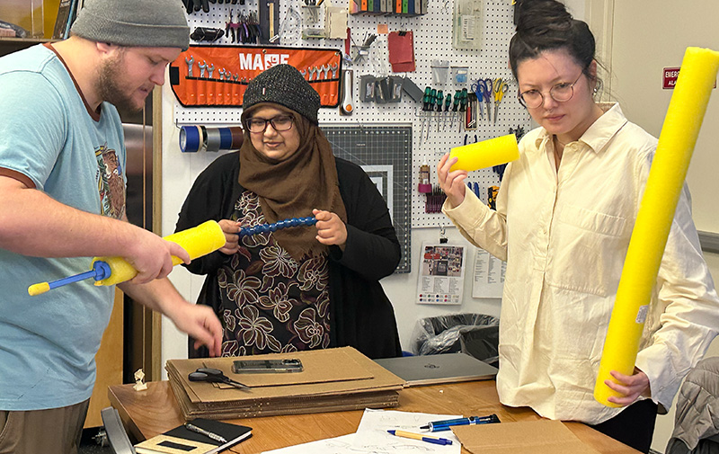 Three adaptation hackfest participants working with foam pool noodles, a flexible tube and a pump to create a prototype portable bidet.