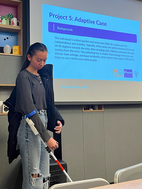 An adaptation hackfest team member presenting a prototype white cane adapted with a cuff and handle for a user with wrist injuries.