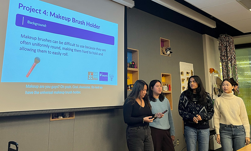 A team of four adaptation hackfest participants presenting the challenge they have addressed: and adaptation for makeup brush handles, which are small and round and tend to roll away.