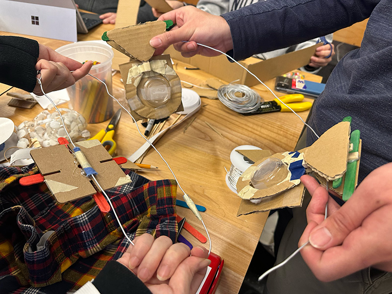 Closeup of a team working on an assistive device for putting on pants. They are using wire, cardboard, tape and various tools. 