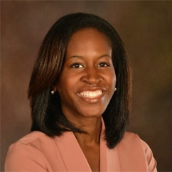 Ebele Okoli, a smiling African American woman with shoulder length hair, wearing a tan blazer.