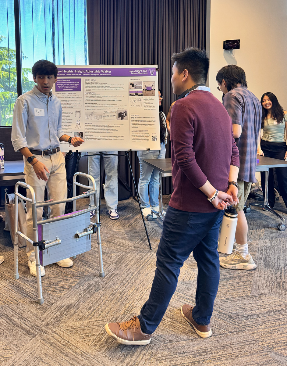 A student stands beside the research poster on a height-adjustable walker with a prototype walker in front. He is in conversation with community members.