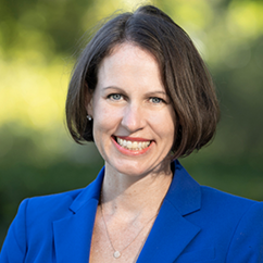 Mary Goldberg, a white woman with short, brown hair. She is wearing a bright blue suit and smiles warmly at the camera.