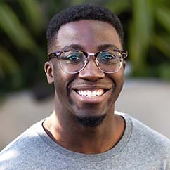 Michael Bervell is a young Ghanaian-American man. He wears horn-rimmed glasses and a grey sweater and a broad smile.