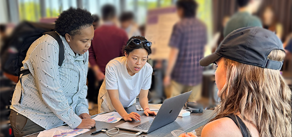 Representatives from one of CREATE's community partners participate in Community Day. The two women are viewing a presentation on a laptop surrounded by research posters and participants.