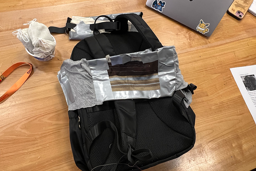 A standard black backpack modified with duct tape, fabric, and padding.