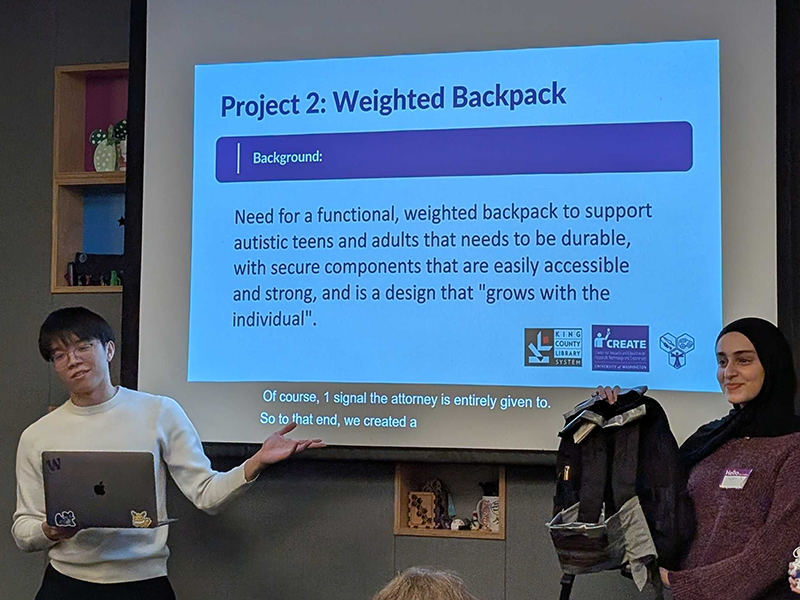 Team members presenting the needs case for a weighted backpack and holding up their prototype made from a standard backpack, tape, and fabric