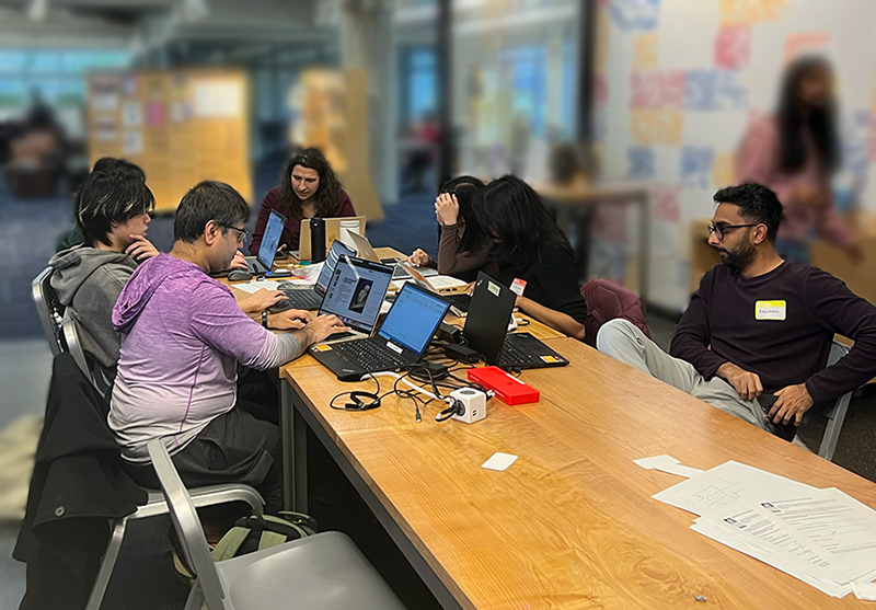 Seven people seated at a work table and focused on their laptops during the prototyping session.