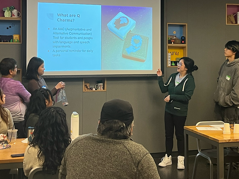 Team members present a slide explaining what Q Charms are.