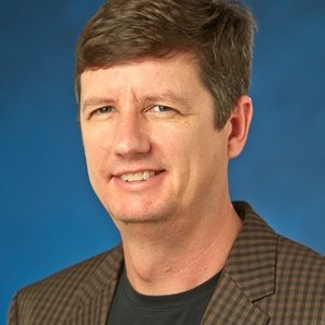 Headshot of Ed Summers, a white man with brown hair, wearing a black t-shirt and a brown and black checked blazer.