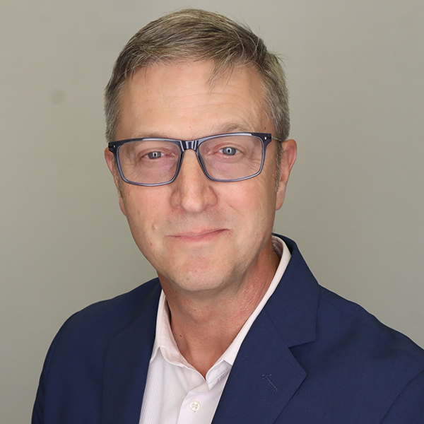 Mark Harniss a white man in his 50s with short brown hair and blue eyes, wearing a blue blazer and collared shirt.