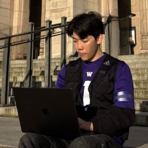 Kris Yu, working on a laptop while sitting on the steps in front of Suzzallo Library.