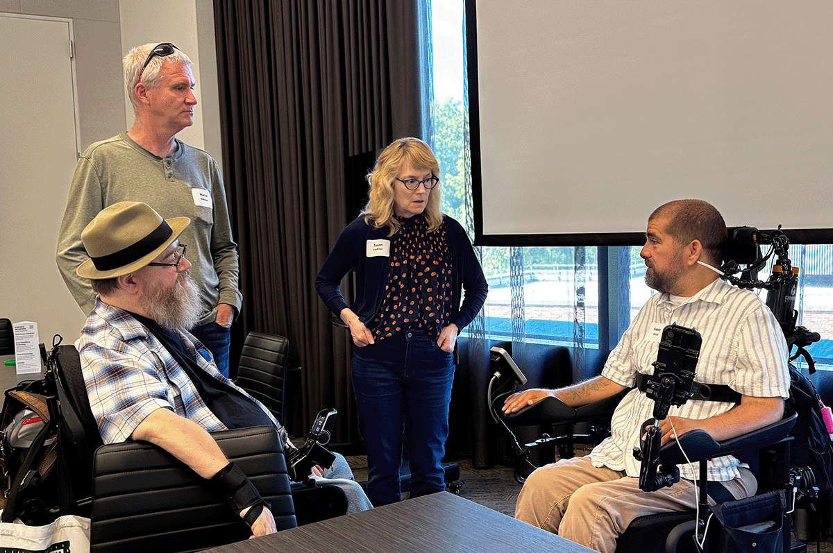 A group of four attendees are gathered in a discussion. Two are using wheelchairs.