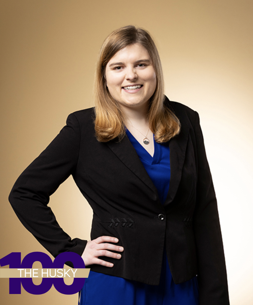 Mia Hoffman, in a photo from her Husky 100 honor, standing with a hand on her hip and dressed in a black suit jacket and blue dress.