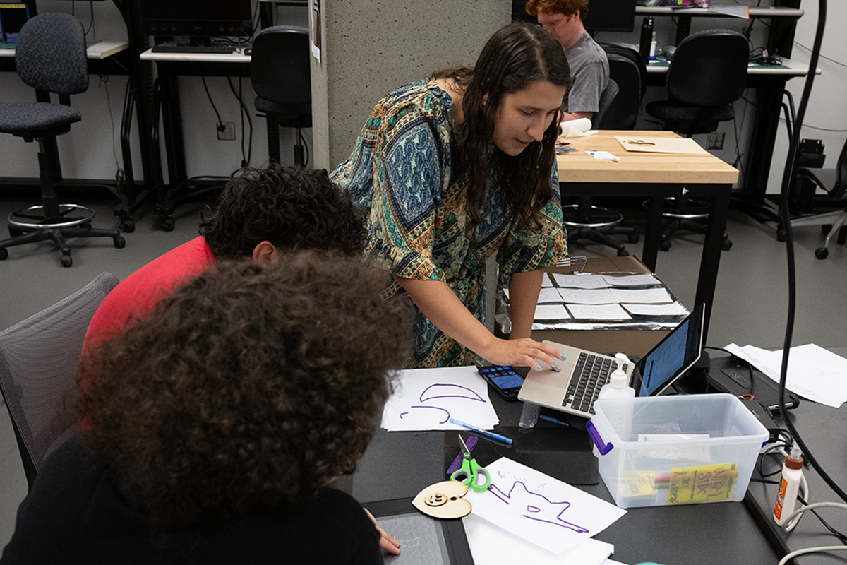 CREATE Ph.D. student Kate Glazko at a laptop, assisting two students.