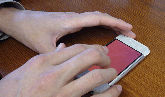 Close-up photo of a person's hands using Slide Rule on a multi-touch smartphone. No information is displayed; the output is auditory.