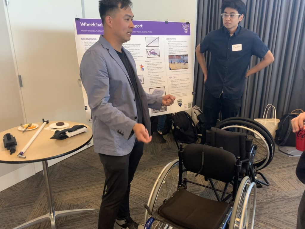 A conversation in front of a student poster with a demonstration wheelchair.