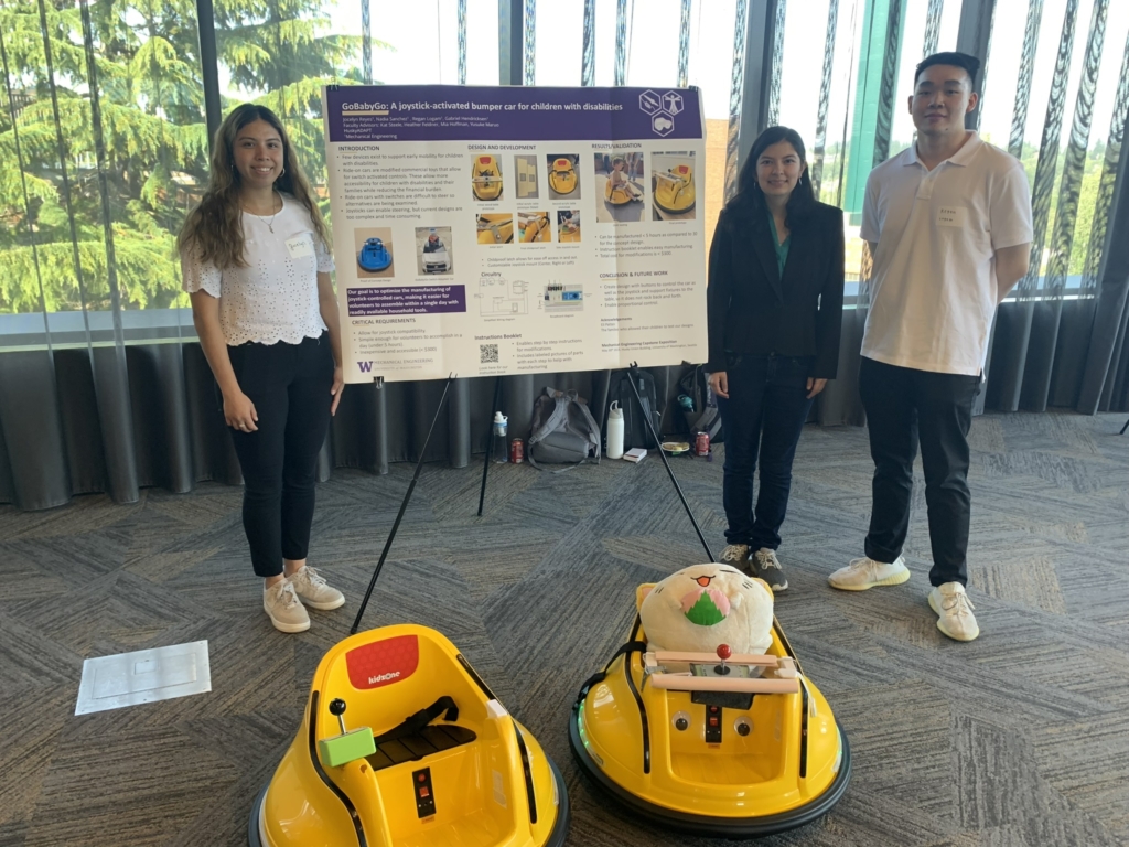 Students stand by their poster with two adaptable ride-on toys.