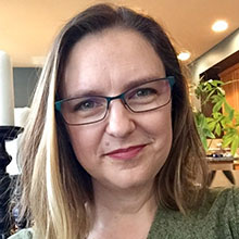 Headshot of Kathleen Q. Voss, a white woman with blonde-brown hair, wearing blue eyeglasses