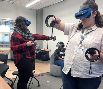 Two student participants at the 2019 OurCS workshop use virtual reality goggles and hand controllers