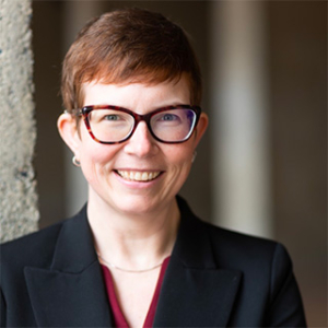 Headshot of Stephanie Kerschbaum, a white woman with short, red hair wearing a suit and pearls