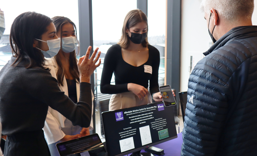 Three student members at the HuskyADAPT table, sharing information and video about the program. 