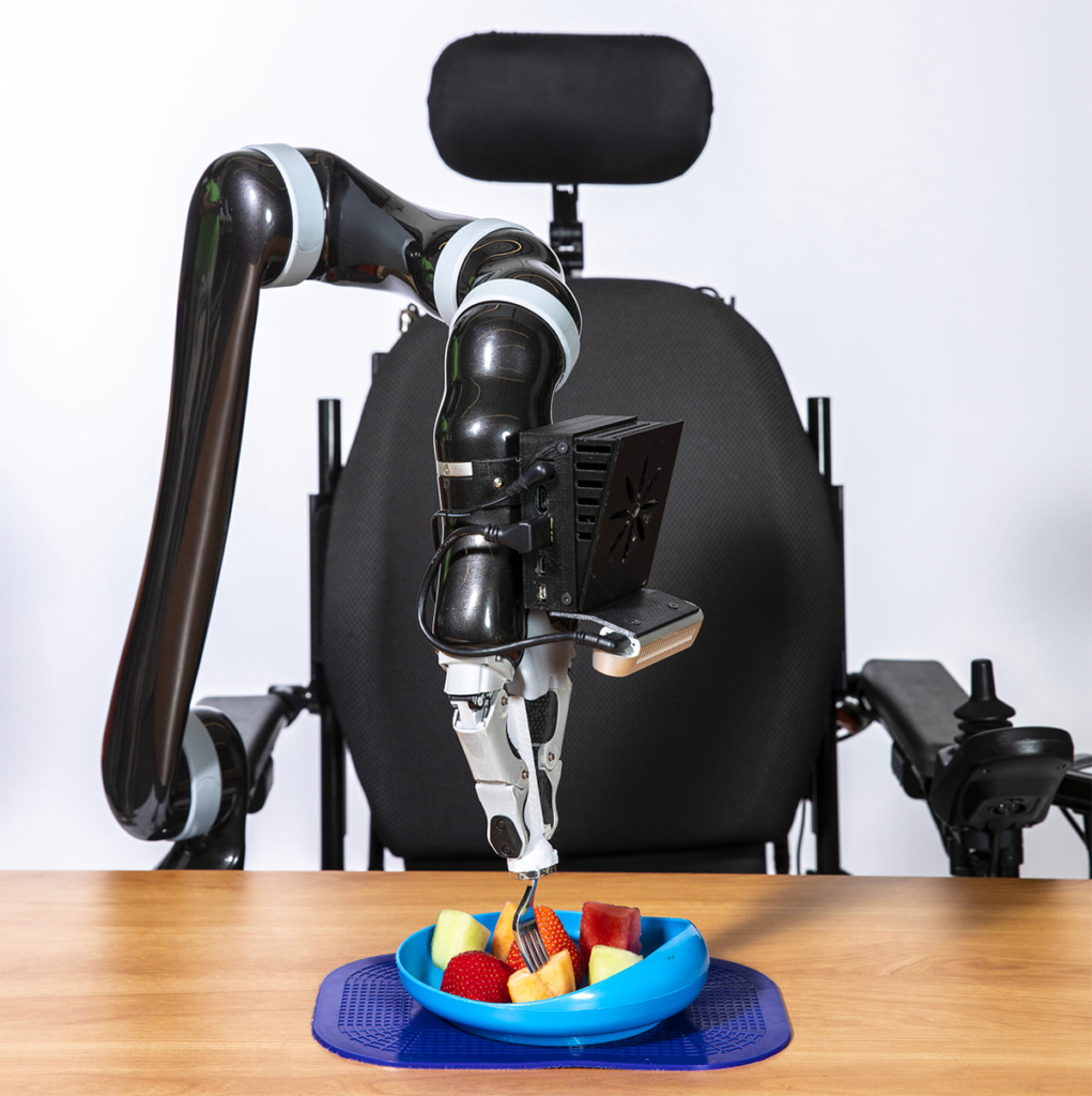 An assistive-feeding robotic arm attached to a wheelchair uses a fork to stab a piece of fruit on a plate among other fruits.