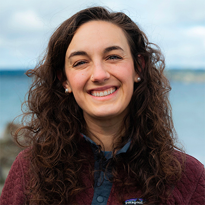 Headshot of Megan Ebers, a young woman with dark wavy hair, smiling broadly.