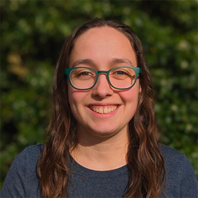 Headshot of Nicole Zaino, a young woman with wavy brown hair and teal eyeglasses.