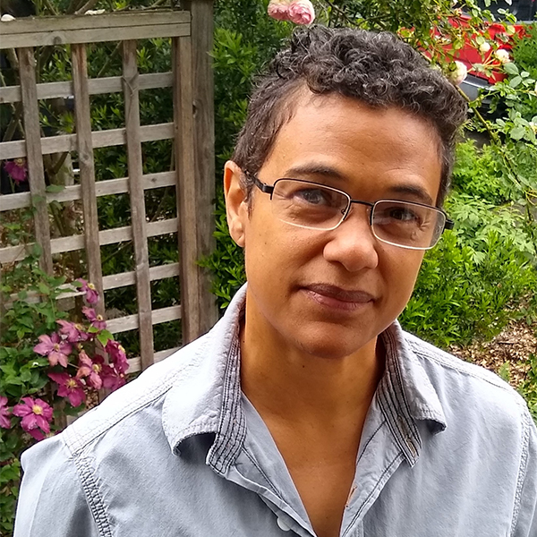 Headshot of Jennifer Stanton, in a casual button-down shirt and standing in front of a garden trellis.