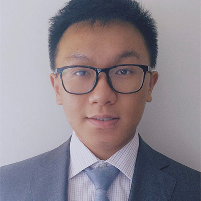 Headshot of Ricky Zhang, a young man with short hair, wearing black frame glasses and a gray business suit.