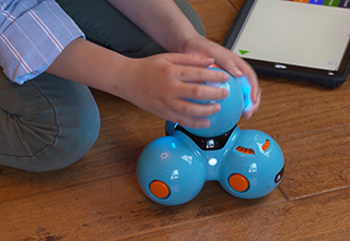 Child holding a toy-like robot that he has programmed with a block coding app
