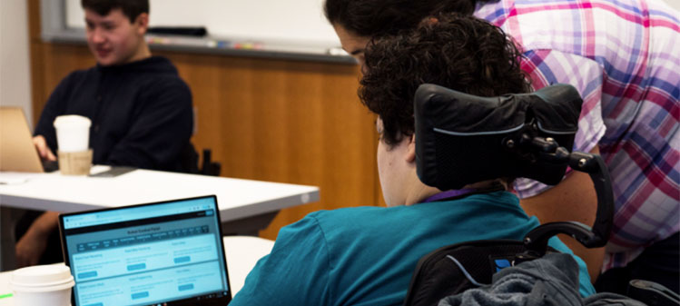 Three students, one using a power wheelchair, use laptops to control robots at the DO-IT Summer Study 2019